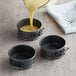 A black metal Wilton mini springform cake pan set with yellow cake batter being poured into three pans.