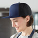 A woman in a professional kitchen wearing a navy blue and black Mercer Culinary trucker hat.