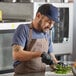 A man in a Mercer Culinary navy blue trucker cap and apron cutting green peppers in a kitchen.