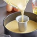 A person using a Wilton cake heating core to pour batter into a cake pan.