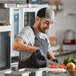A man wearing a Mercer Culinary trucker cap and apron cutting vegetables in a kitchen.