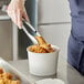 A person using tongs to put fried chicken in a white Choice food bucket.