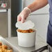 A person in gloves putting fried chicken in a white Choice food bucket.