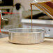 A person pouring liquid into an American Metalcraft aluminum round cake pan on a table.