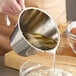 A person using a Linden Sweden stainless steel measuring cup to pour liquid into a bowl.
