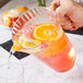 A person pouring a glass of orange juice into a WNA Comet Classic Crystal pitcher.