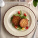 A Carlisle sweet cream melamine plate with two meat patties and salad on it.