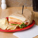 A sandwich wrapped in Bagcraft Packaging EcoCraft deli paper with chips on a red plate.