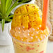 A cup of mango bubble tea with Bossen Chili Pepper Bursting Boba and a straw on a white background.