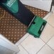 A green and black Bissell upright vacuum cleaner on the floor in a room with a diamond patterned carpet.