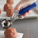 A person using a Hamilton Beach blue metal scoop to make meatballs.