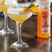 A glass of peach drink on a table with a bottle of Master of Mixes Peach Syrup.