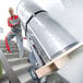 A man using a Magliner powered stair climbing hand truck to carry a large metal cylinder up stairs.