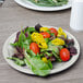 A Carlisle bone melamine salad plate with lettuce, tomatoes, and peppers.