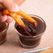 A person dipping a french fry into a glass of AAK Grill Blazin' BBQ sauce.