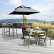 A Grosfillex Java taupe resin sidechair with wicker back on a patio with a table and chairs and an umbrella.