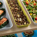 A yellow Cambro market pan on a table with food in it.