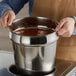 A person holding a Thunder Group vegetable inset pot of liquid over a stove.