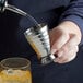 A person using a Franmara stainless steel measuring jigger to pour liquid into a glass