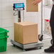A person weighing a brown box on an AvaWeigh digital receiving bench scale.