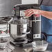 A man pouring liquid into a black Avantco countertop mixer on a counter in a professional kitchen.