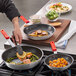 A person using a Choice red aluminum frying pan to cook potatoes and sausage.