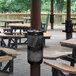 A picnic table with a black Ex-Cell Kaiser Landscape Series 10 gallon round waste receptacle with a black lid.