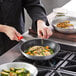 A person cooking food in a Choice aluminum non-stick fry pan.