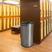 A stainless steel Ex-Cell Kaiser round towel receptacle in a room with lockers.