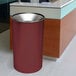 A burgundy Ex-Cell Kaiser Premier Series trash can on a white counter.