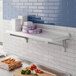 A white Cambro Camshelving wall shelf in a kitchen with purple boxes on it.