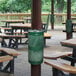 A picnic area with picnic tables and a Ex-Cell Kaiser hunter green waste receptacle on a table.
