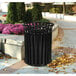 A black Ex-Cell Kaiser Streetscape outdoor trash receptacle on a sidewalk.