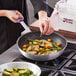 A person cooking food in a Choice aluminum non-stick fry pan with a purple allergen-free silicone handle.