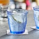 A close-up of a Duralex blue glass with ice and a lemon in it.