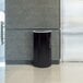 A black Ex-Cell Kaiser Kaleidoscope half round trash receptacle with a wall behind it.