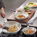 A person cooking brussels sprouts in a Choice aluminum frying pan.