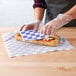 A person wearing plastic gloves putting a sandwich in blue checkered deli wrap.