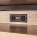 A close-up of a Safco black daisy chain power module on a wood surface.