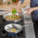 A woman frying a fried egg in a Vollrath stainless steel fry pan on a stove.