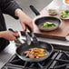 A person cooking meat and potatoes in Vollrath Wear-Ever frying pans on a stove.