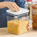 A person using an OXO Good Grips square container with a white lid to store pasta.