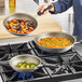 A person cooking food in three Vollrath Wear-Ever non-stick frying pans on a stove.