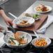 A person cooking salmon and asparagus in a Vollrath frying pan.