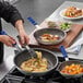 A man cooking food in a Vollrath Wear-Ever frying pan with blue Cool handle.