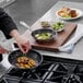 A person cooking brussels sprouts and mushrooms in a Vollrath Optio frying pan.