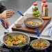 A person using a Vollrath Wear-Ever frying pan to cook vegetables on a stove.