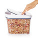 A hand using a white OXO food storage container to scoop cereal.