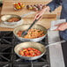 A woman cooking pasta in a Vollrath Wear-Ever frying pan on a stove.