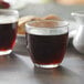 Two Duralex glass tumblers filled with brown liquid on a table in a coffee shop.